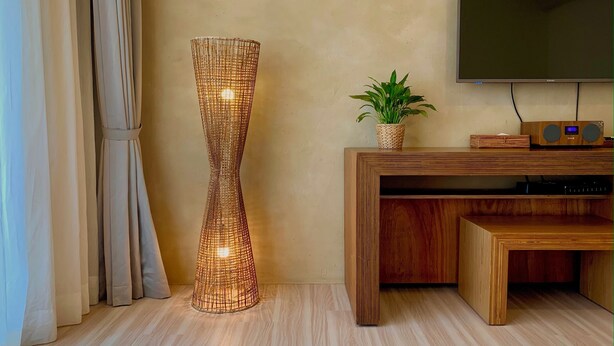 Una sala de estar moderna con una lámpara de pie alta de fibras tejidas, un mueble de madera para entretenimiento con televisor de pantalla plana y una planta en maceta.