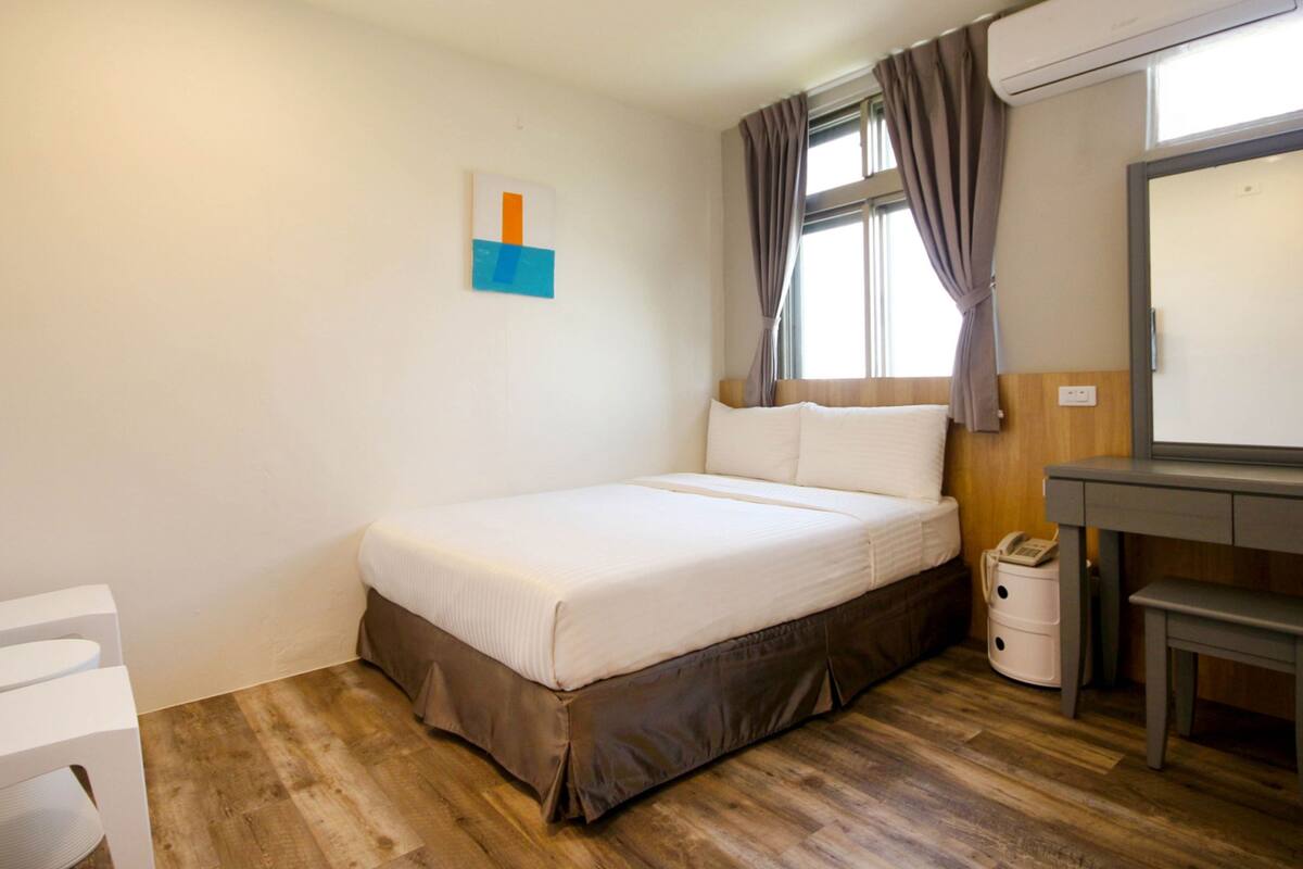 Un dormitorio con cama, escritorio, silla, teléfono y ventana con cortinas.
