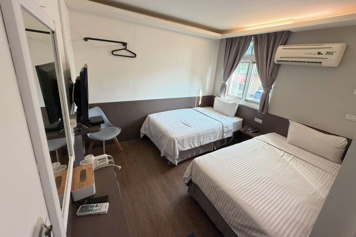 Habitación de hotel con dos camas, un escritorio, una silla, un televisor y un aire acondicionado.