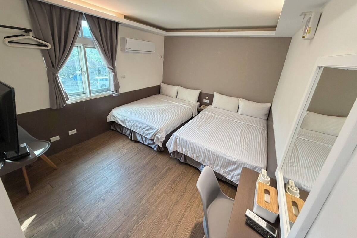 Habitación de hotel con dos camas, un escritorio, una silla, un televisor y una ventana con cortinas.