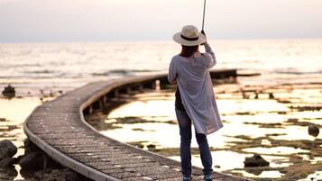 A person standing on a curved wooden boardwalk by the sea, wearing a hat and jeans.