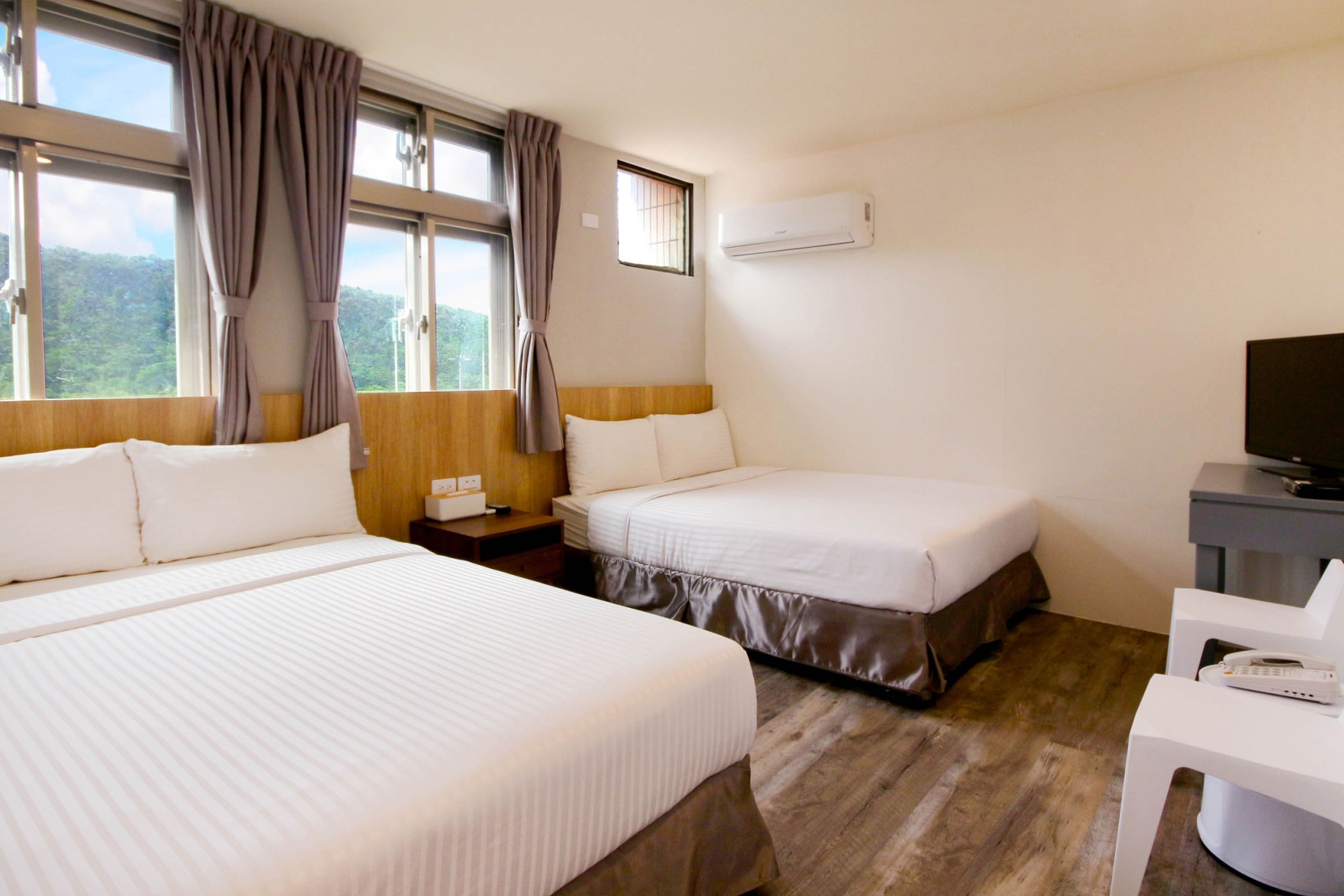A hotel room with two beds, a desk, a chair, an air conditioner, and a window with curtains.