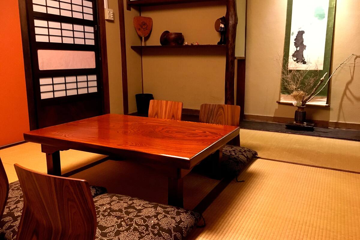 Une pièce de style japonais traditionnel, avec un sol recouvert de tatamis, une table à manger en bois et de petites chaises en bois.