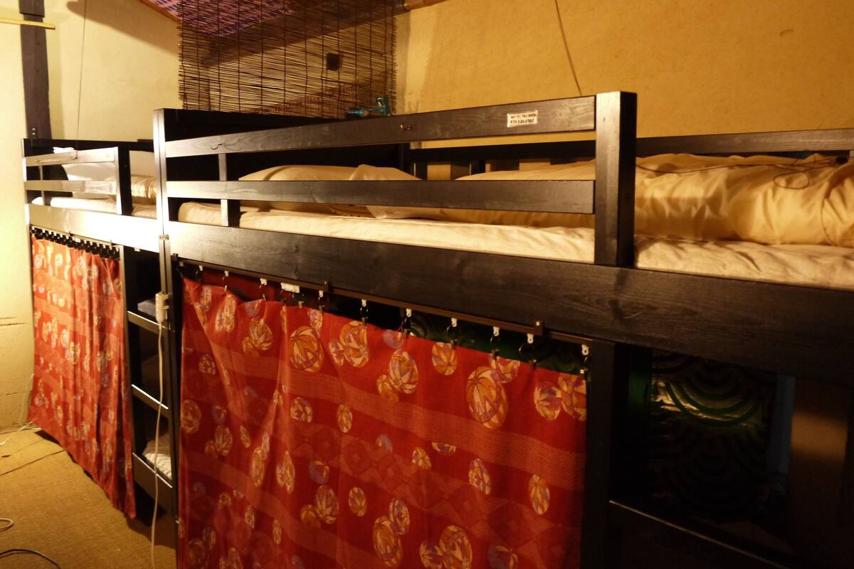 Un lit superposé avec une structure en métal et un rideau rouge.