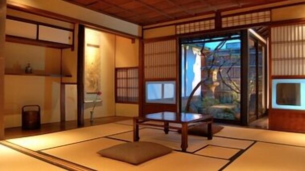 Une pièce de style japonais traditionnel, avec un sol recouvert de tatamis, une petite table en bois et des portes coulissantes donnant sur une vue d’un bâtiment traditionnel.