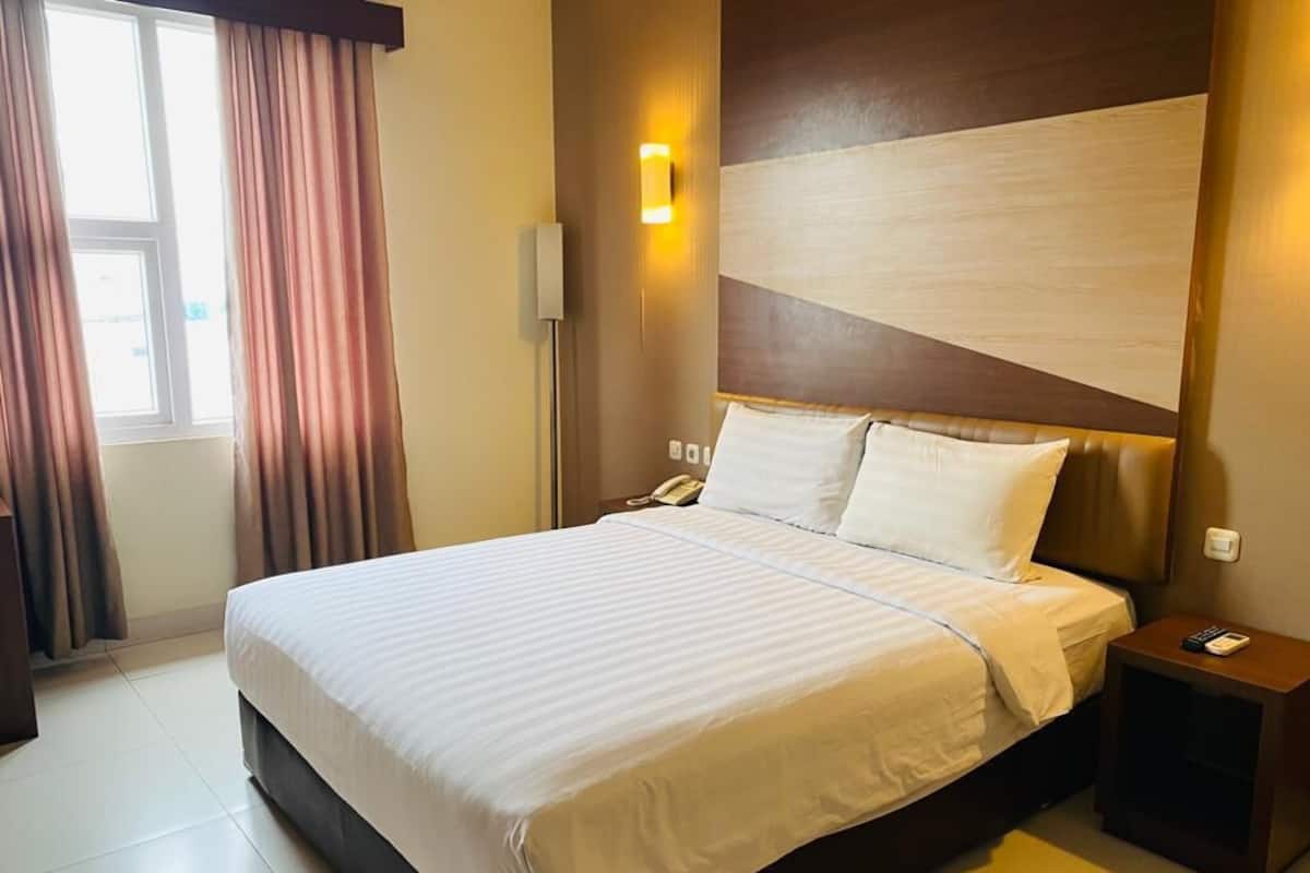 A hotel room with a large bed, a bedside table with a lamp, and a window with curtains.