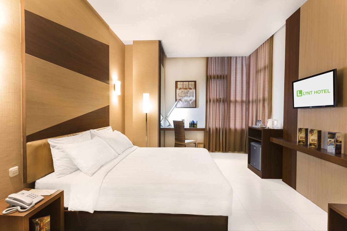 A hotel room with a large bed, a desk with a chair, a television, and a minibar.