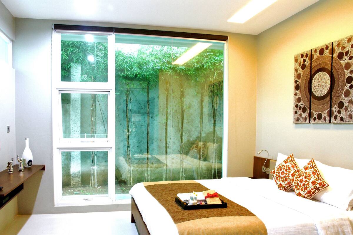A hotel room with a bed, a TV, a desk, and a sliding glass door to a garden.