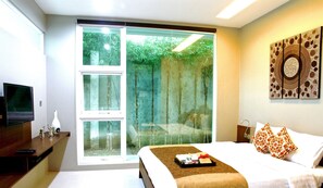 A hotel room with a bed, a TV, a desk, and a sliding glass door to a garden.