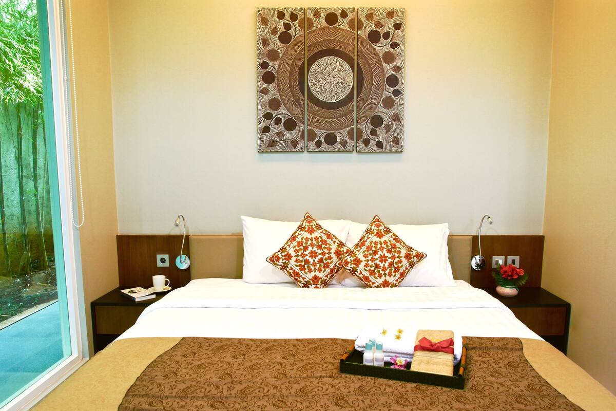 A hotel room with a large bed, two nightstands, a window with a view of trees, and a wall art piece.