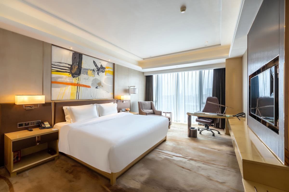 Une chambre d’hôtel avec un grand lit, un bureau, une chaise, une télévision et un tableau au mur.