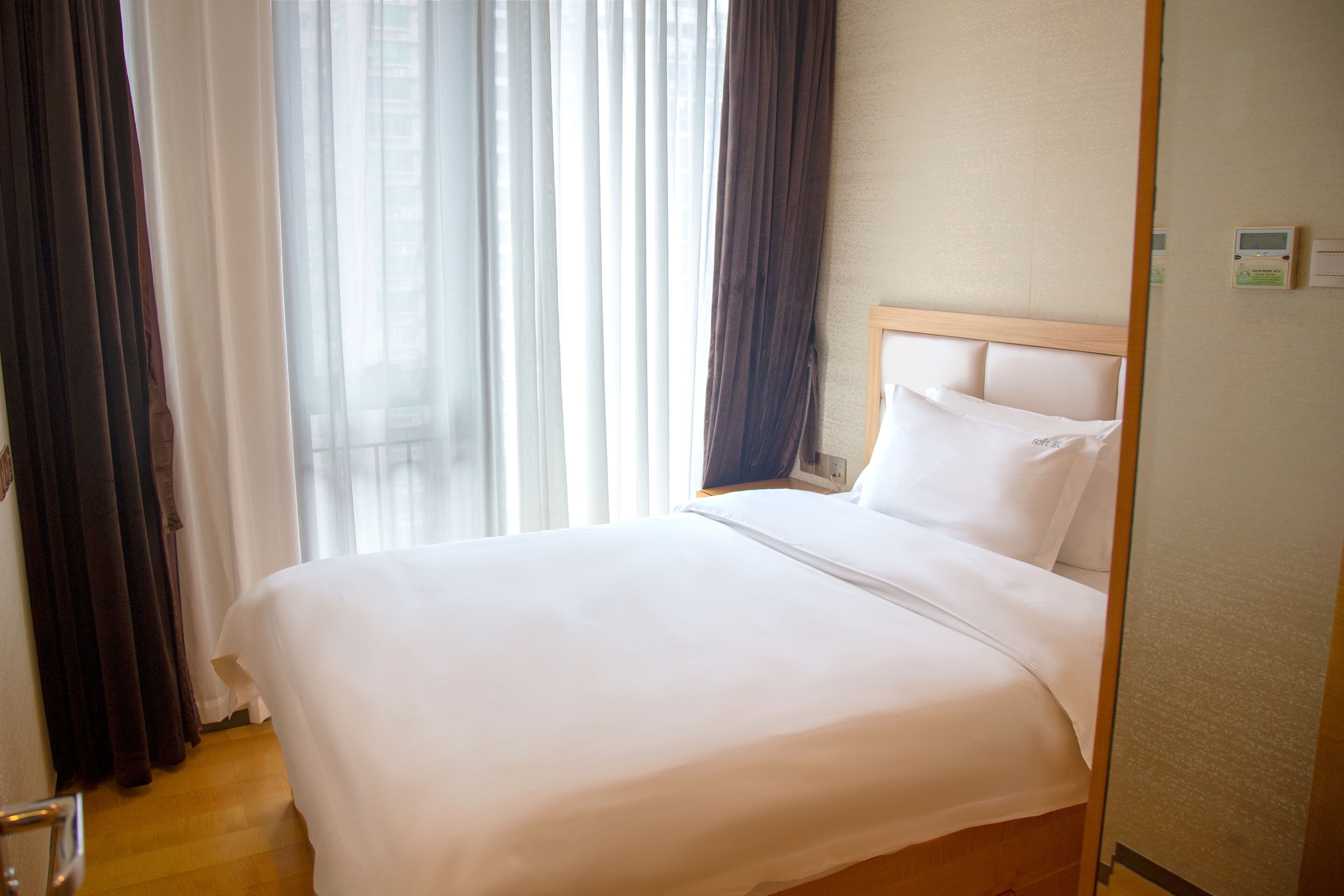 A hotel room with a large bed, a wooden headboard, and a window with sheer curtains.