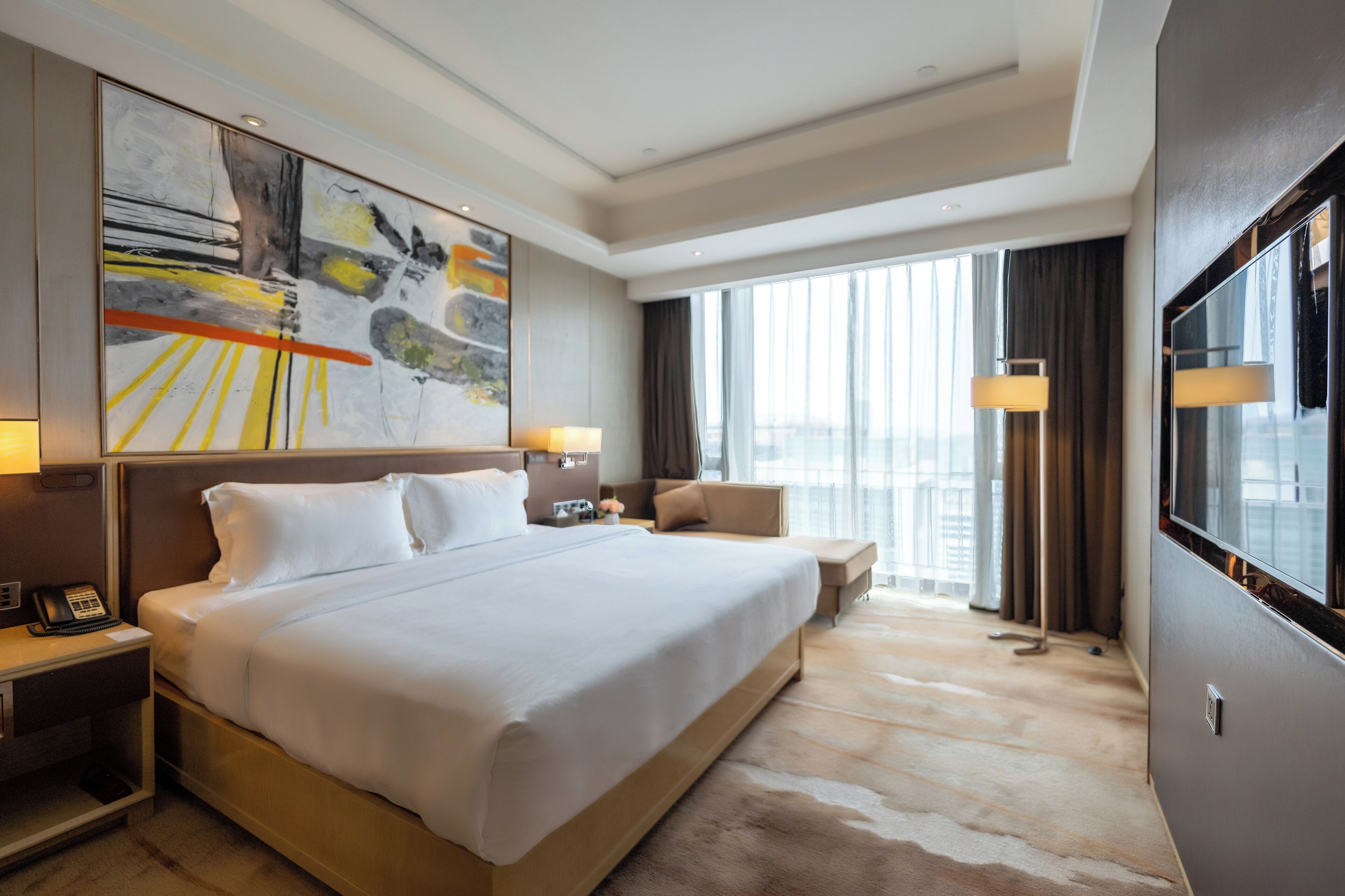 A modern hotel room with a large bed, bedside tables, a desk, and a large window offering a city view.