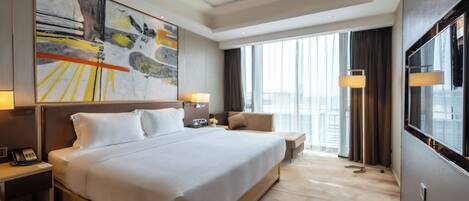 A modern hotel room with a large bed, bedside tables, a desk, and a large window offering a city view.