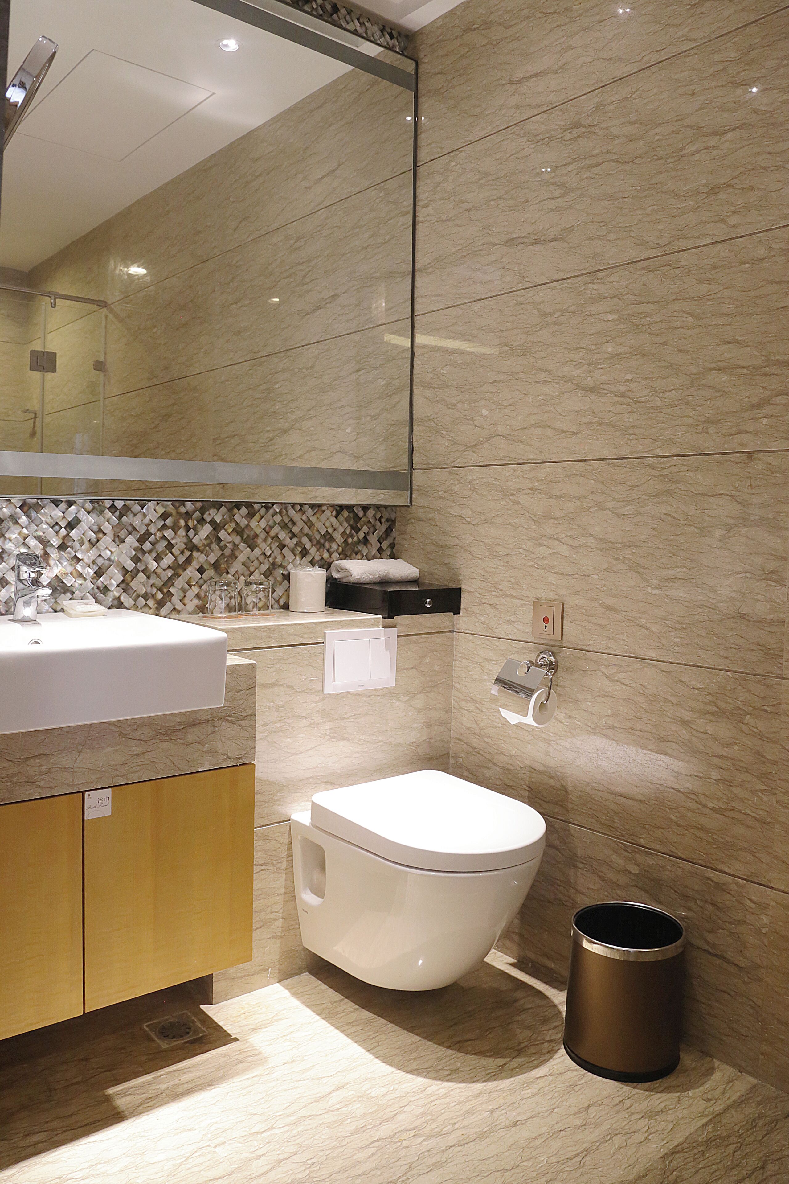 A modern bathroom with a marble sink, a toilet, and a trash can.