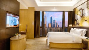 A hotel room with a large bed, a TV mounted on the wall, a desk, and a view of the city skyline.