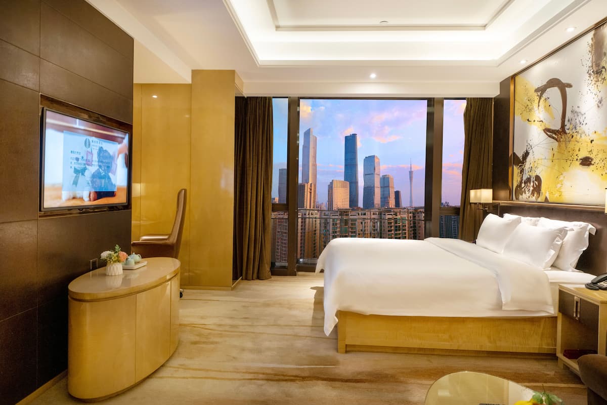 Une chambre d’hôtel avec un grand lit, un téléviseur fixé au mur, un bureau et une vue sur le panorama urbain.