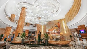 A spacious lobby with high ceilings, marble columns, a central fountain, and a large mural.