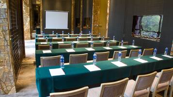 A conference room with rows of tables and chairs, water bottles, and a projector screen.