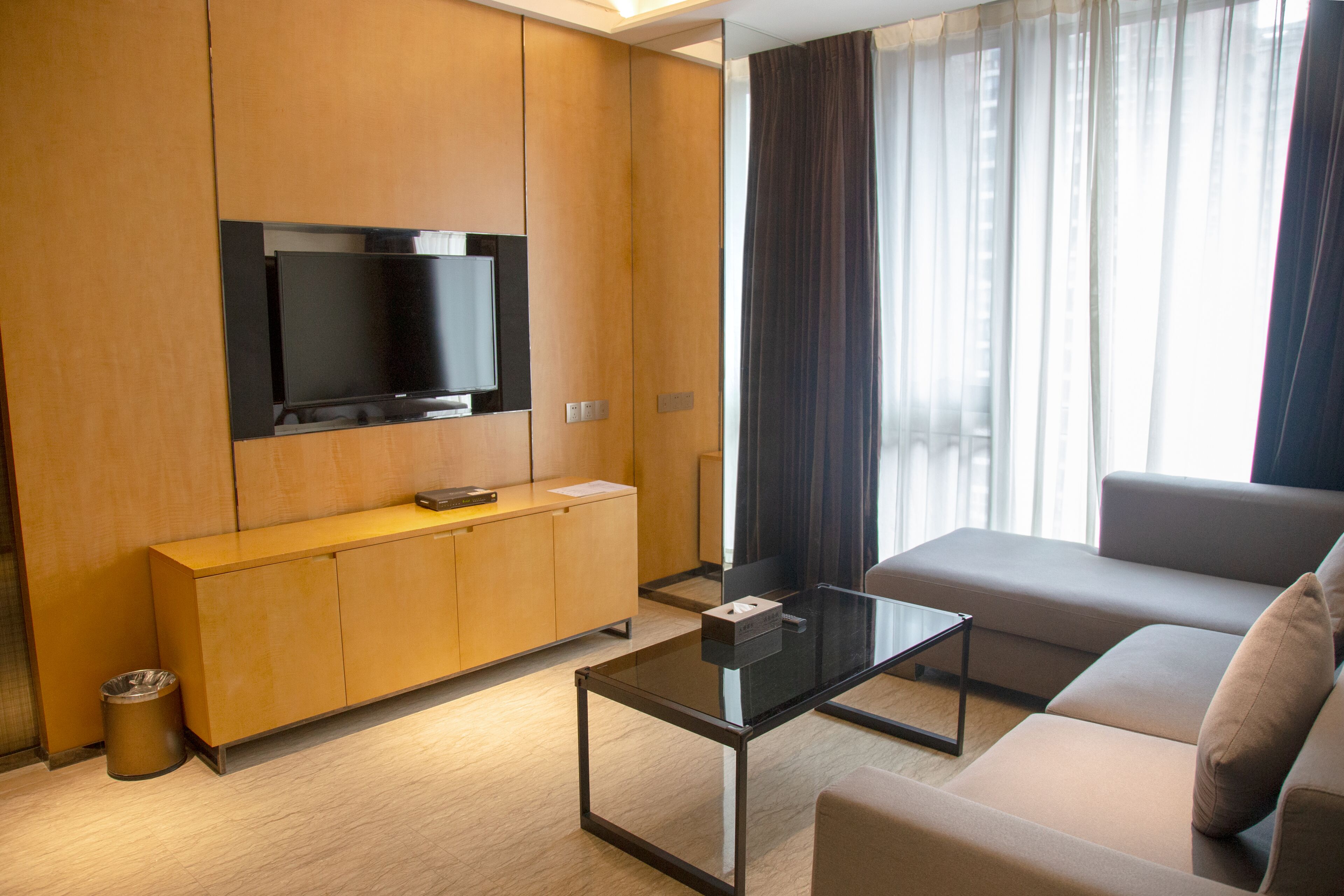 A modern living room with a flat-screen TV mounted on a wooden cabinet, a glass coffee table, and a sofa.