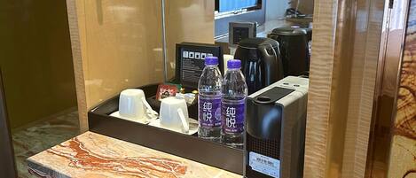 A hotel room with a marble countertop, a coffee machine, bottled water, and a tea set on a shelf.