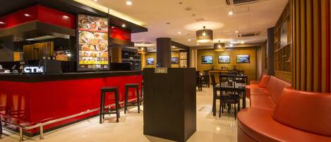 A modern restaurant with a red counter, black stools, and a seating area with a red couch.
