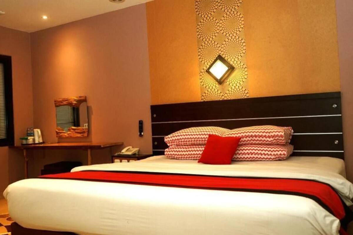 A hotel room with a large bed, a desk with a telephone, and a wall-mounted mirror.