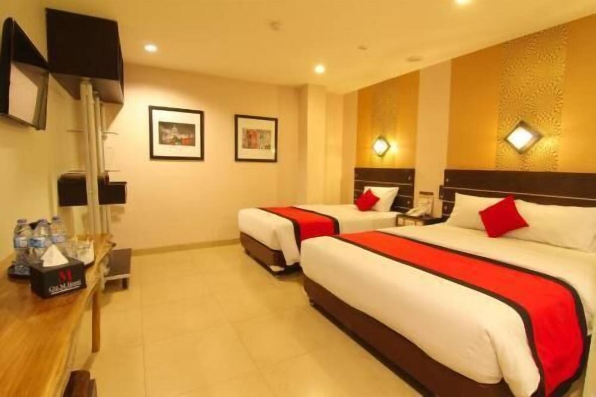 A hotel room with two beds, a desk with a lamp, and framed pictures on the wall.