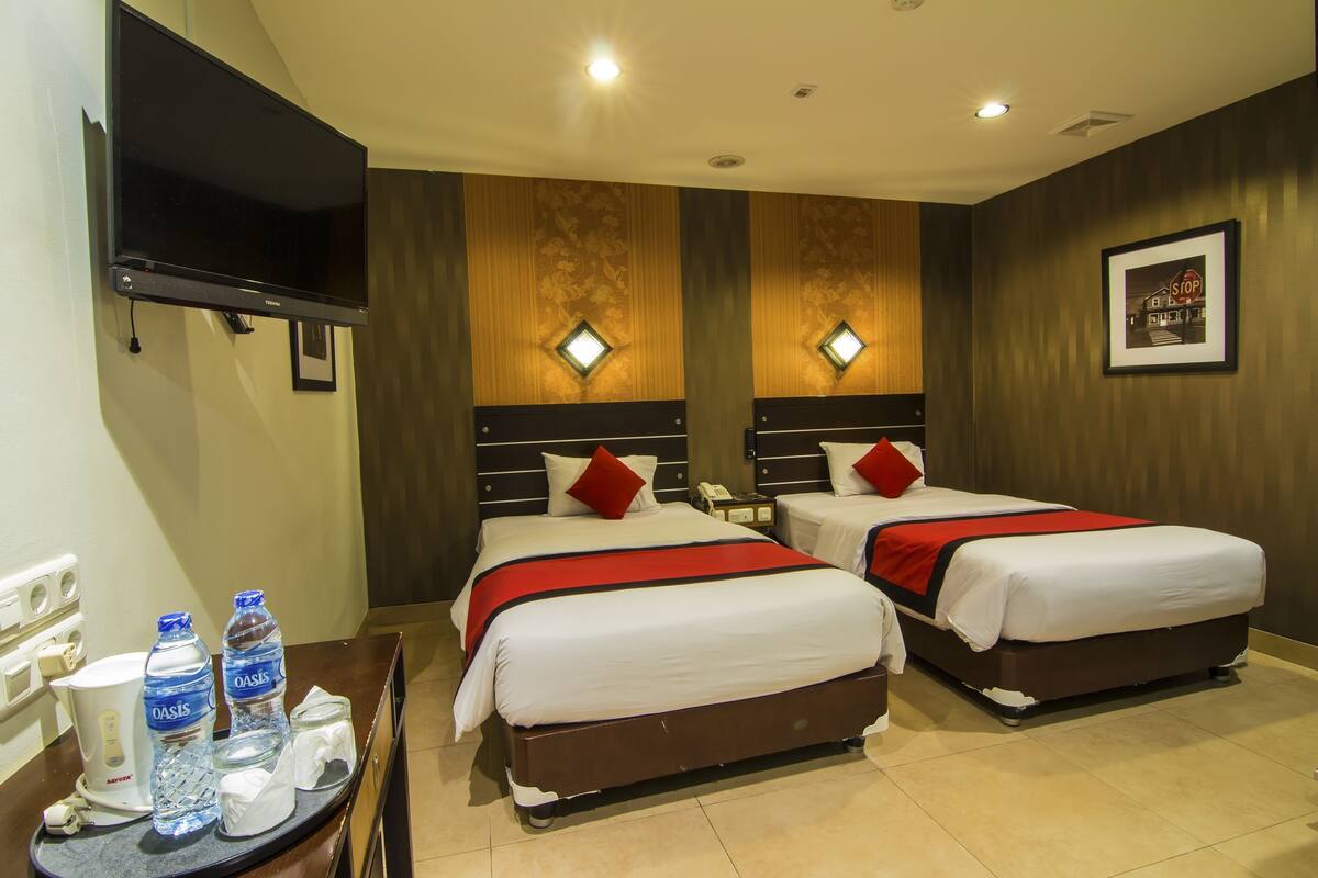 A hotel room with two beds, a TV, a desk with a coffee maker, and two water bottles.