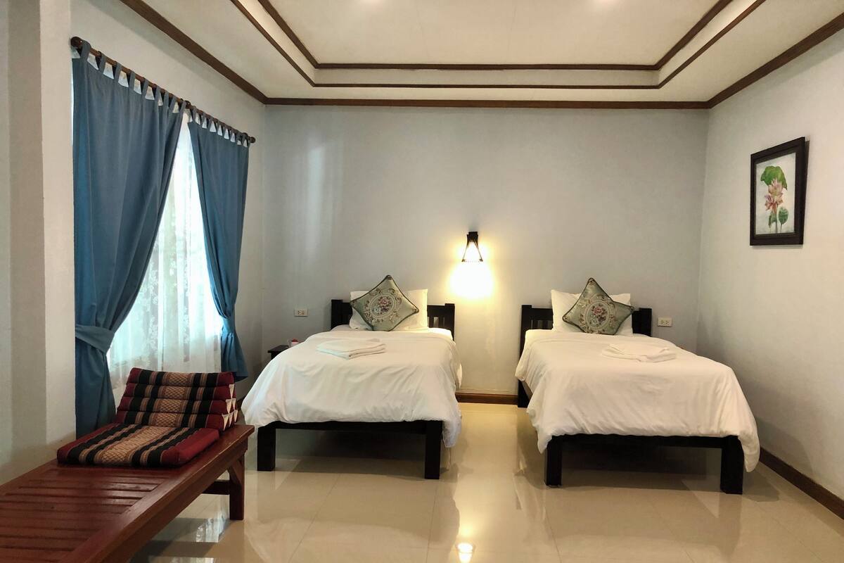 A hotel room with two beds, a bench, a wall-mounted light, and a framed picture.