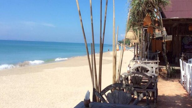 Een strandsetting met een houten tafel, een rieten dakgebouw en uitzicht op de oceaan.