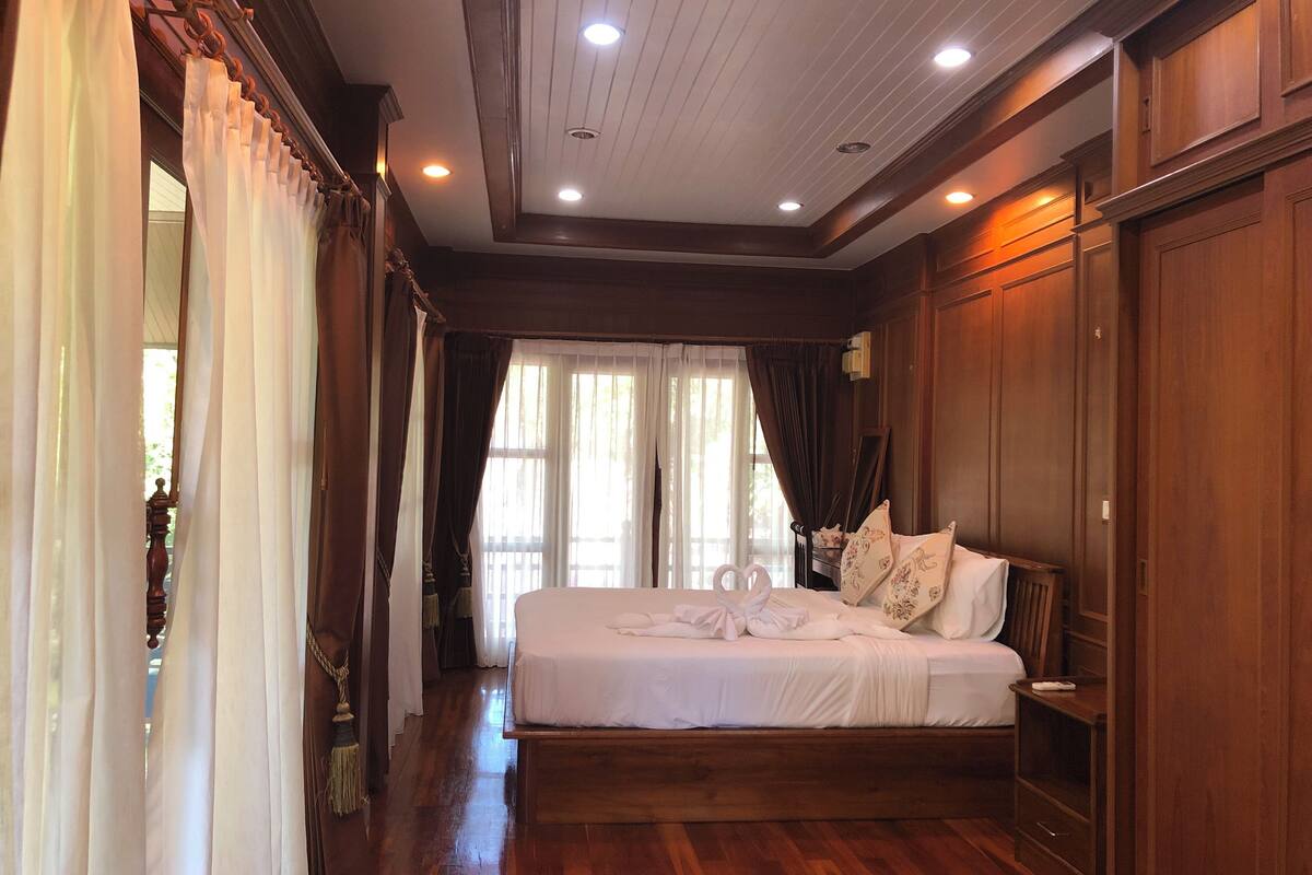 A hotel room with a wooden bed, a nightstand, and a large window with curtains.