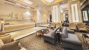 Un hall d’entrée spacieux comprenant un comptoir d’accueil, un espace salon et des éléments décoratifs, tels qu’un mur représentant un paysage urbain et un revêtement de sol à motifs.