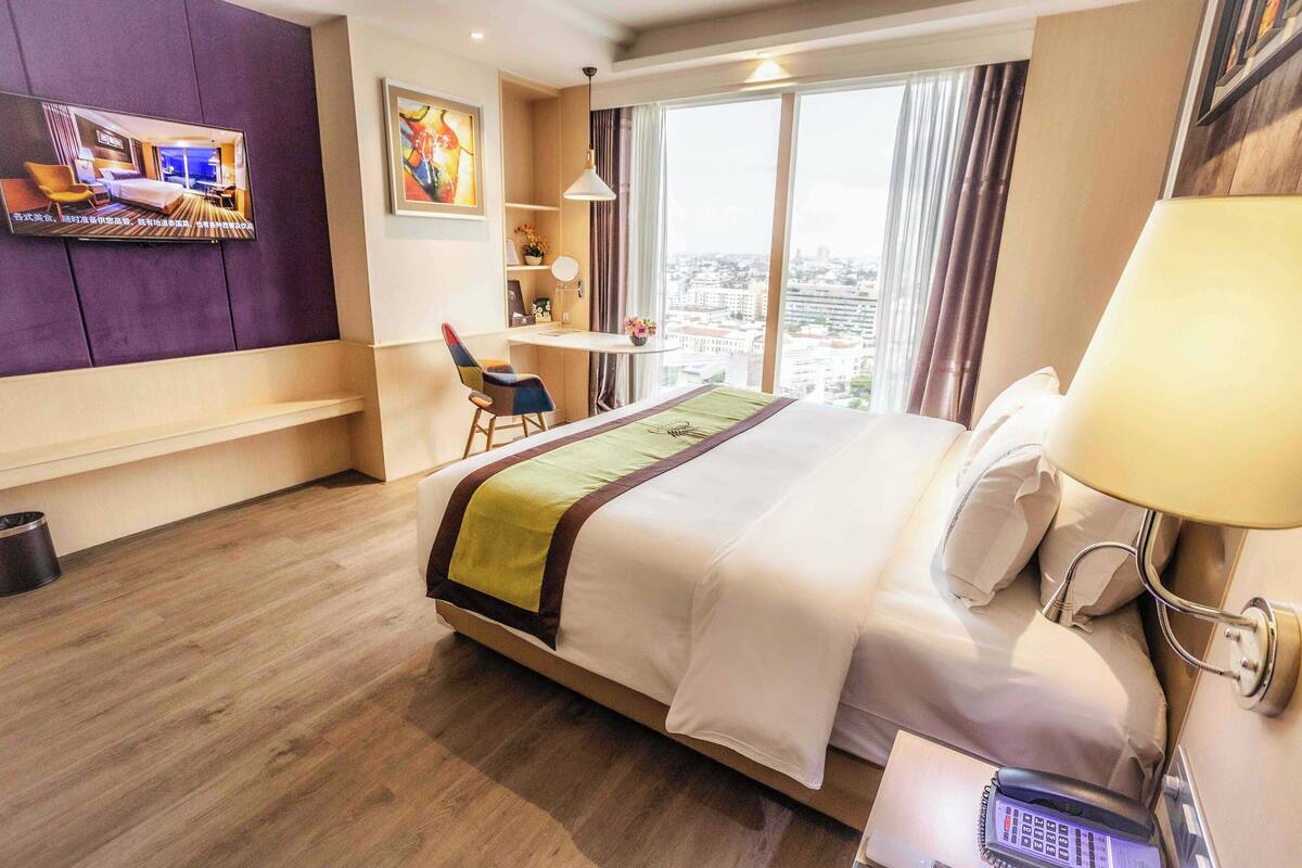 A hotel room with a bed, a desk, a chair, a TV, and a city view.