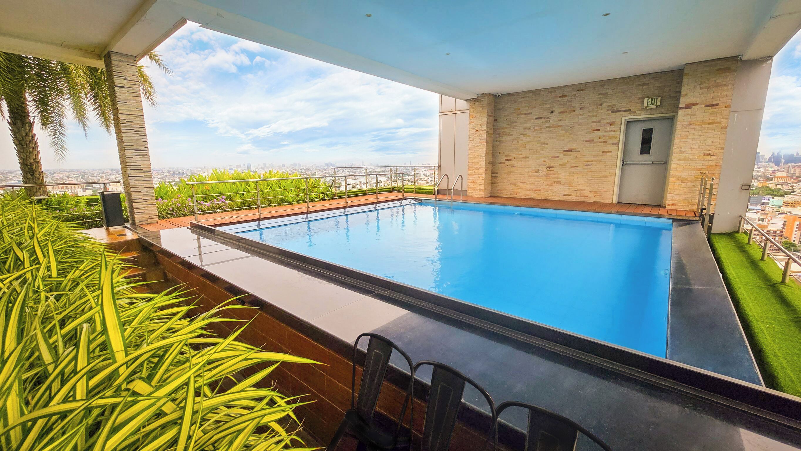 A rooftop swimming pool with a city view, a door marked "EXIT", and a small garden area with plants.