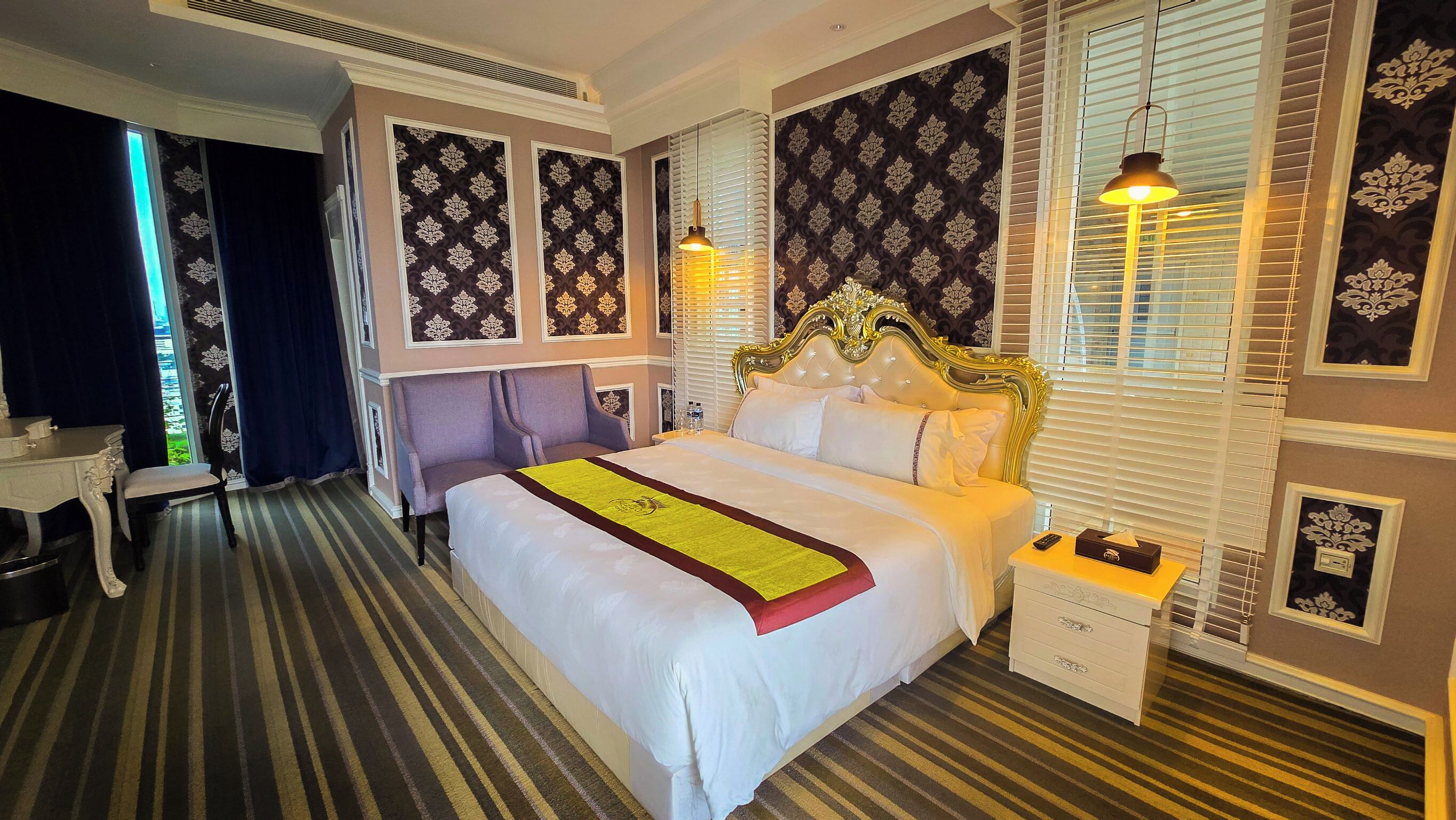 Habitación de hotel con una cama grande, una mesita de noche, una silla, un escritorio y una ventana con persianas.