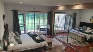 A modern hotel room with a large bed, a sofa, a mirror, and a view of the outdoors. - Moonflower Cottages (Randburg)