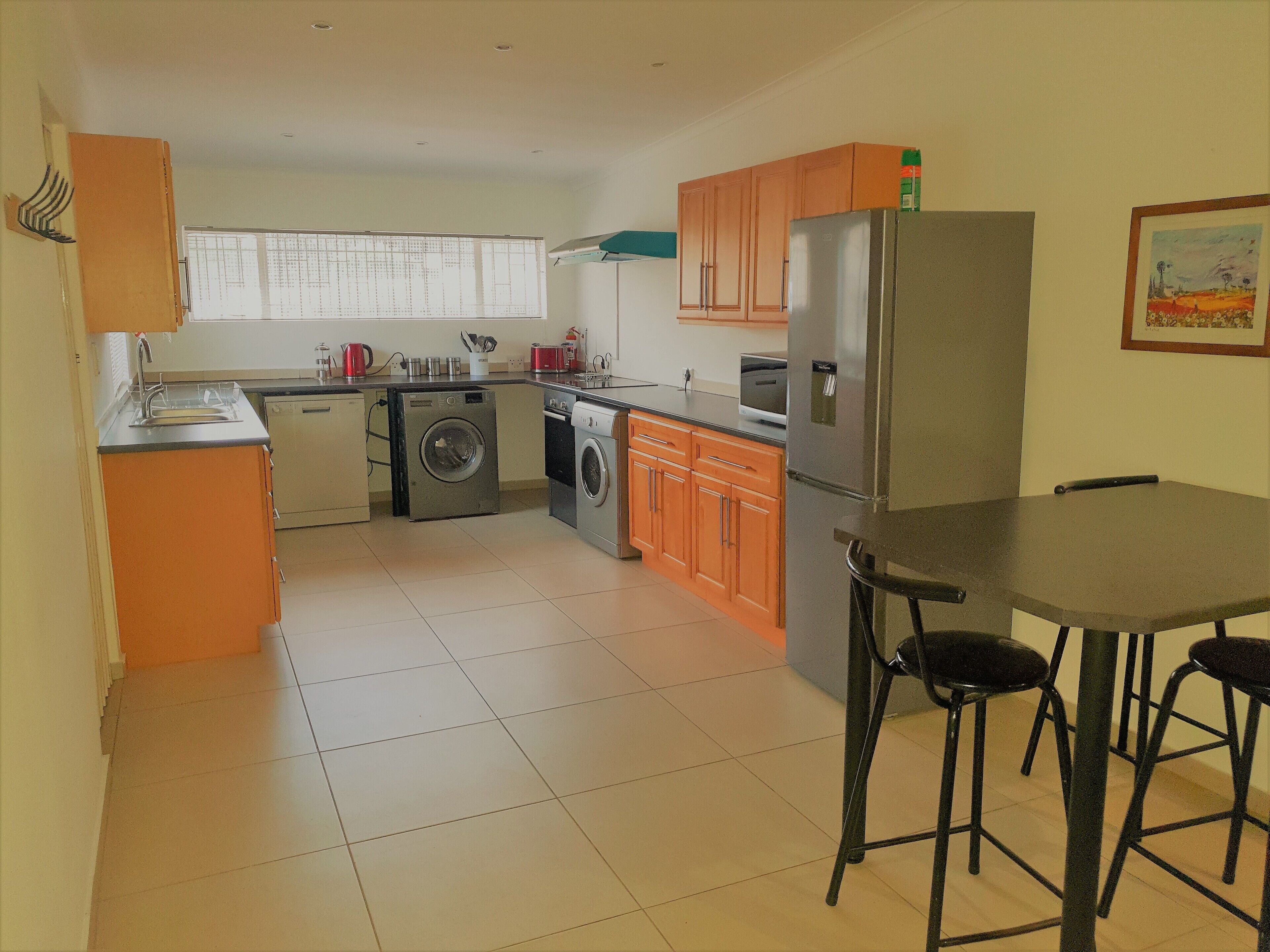 A compact kitchen with a washing machine, a refrigerator, and a dining area with stools.