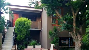 A patio area with a dining table and chairs, a staircase, and a large tree. - Moonflower Cottages (Randburg)