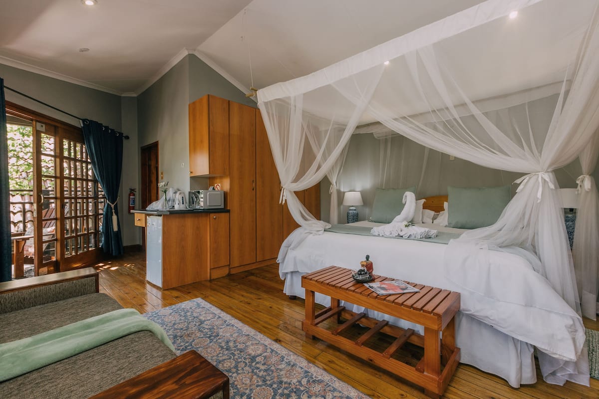 A bedroom with a canopy bed, wooden furniture, and a small kitchenette.