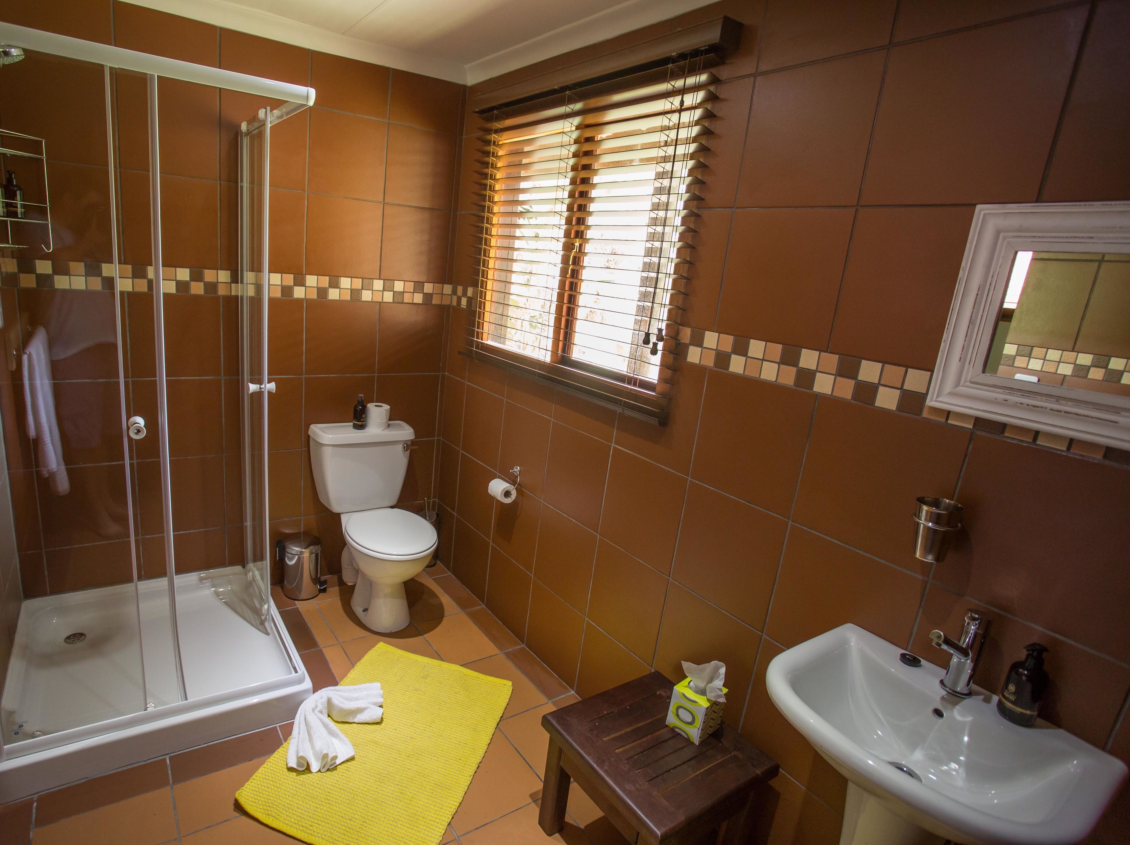 A bathroom with a shower, toilet, sink, and a window with blinds.
