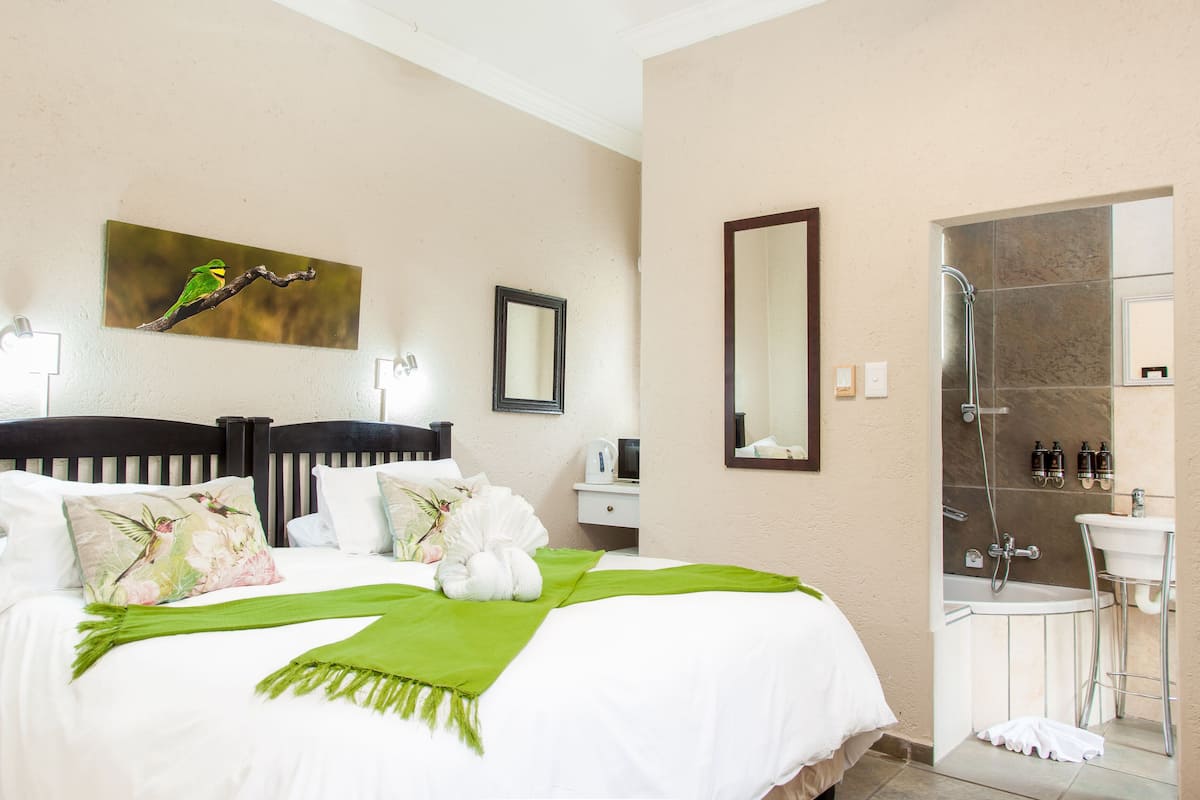 A hotel room with a bed, a painting of a bird on a branch, a bathroom with a shower, and a sink.