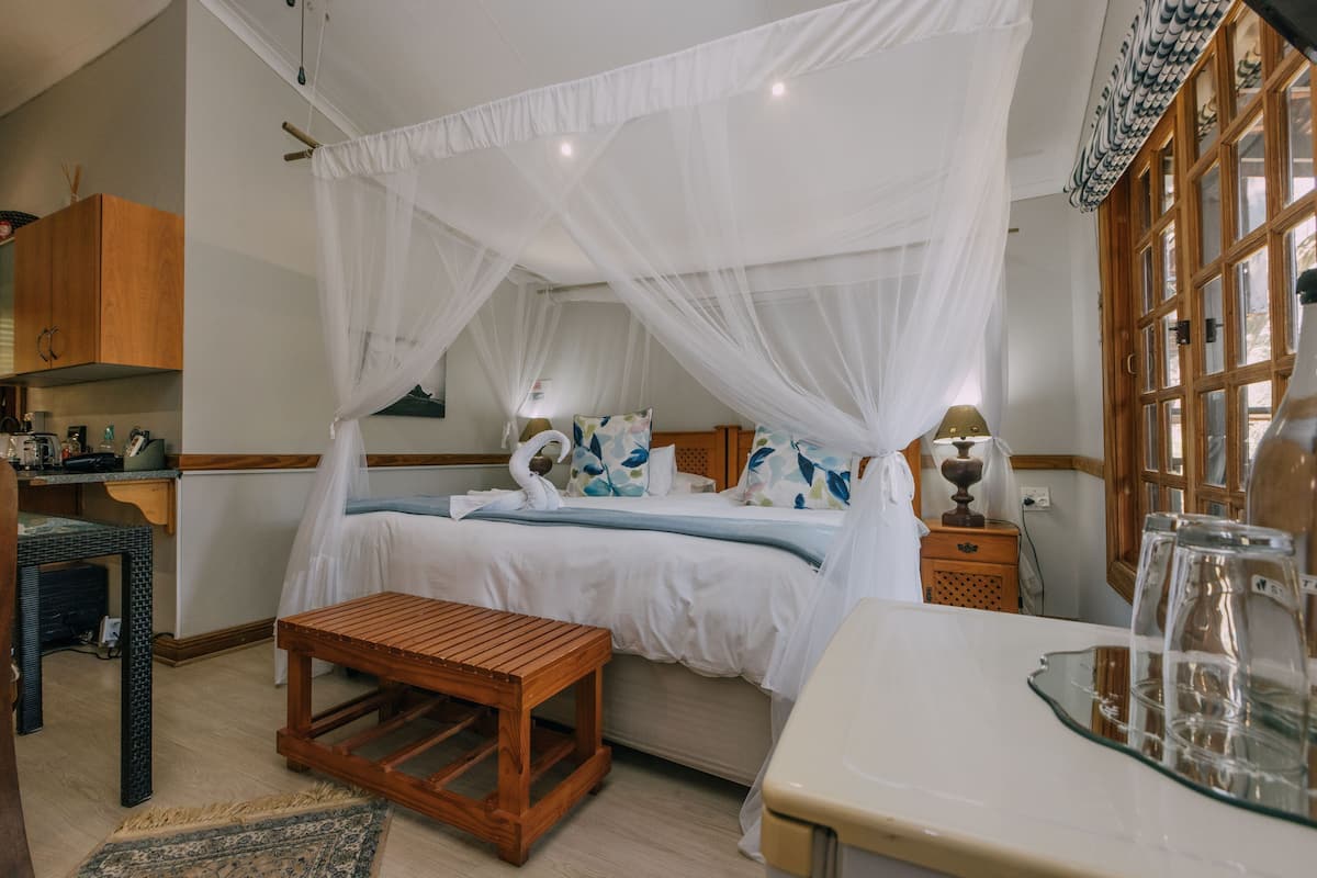 A bedroom with a canopy bed, bedside tables, a wooden stool, and a glass-topped table.