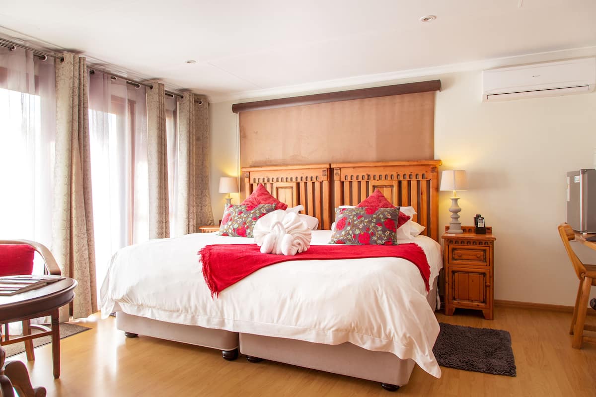 A hotel room with a large bed, a wooden headboard, a nightstand with a lamp, a TV, and a chair.