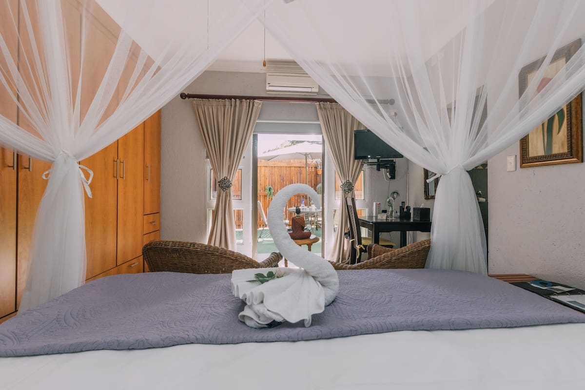 A bedroom with a bed, a wicker chair, a small table, and a view of the outside.