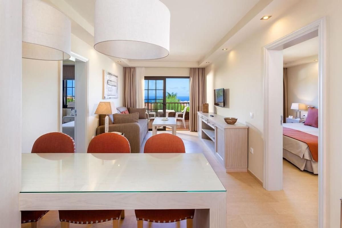 Une chambre d’hôtel avec un coin repas, un canapé, une télévision et un balcon avec vue.