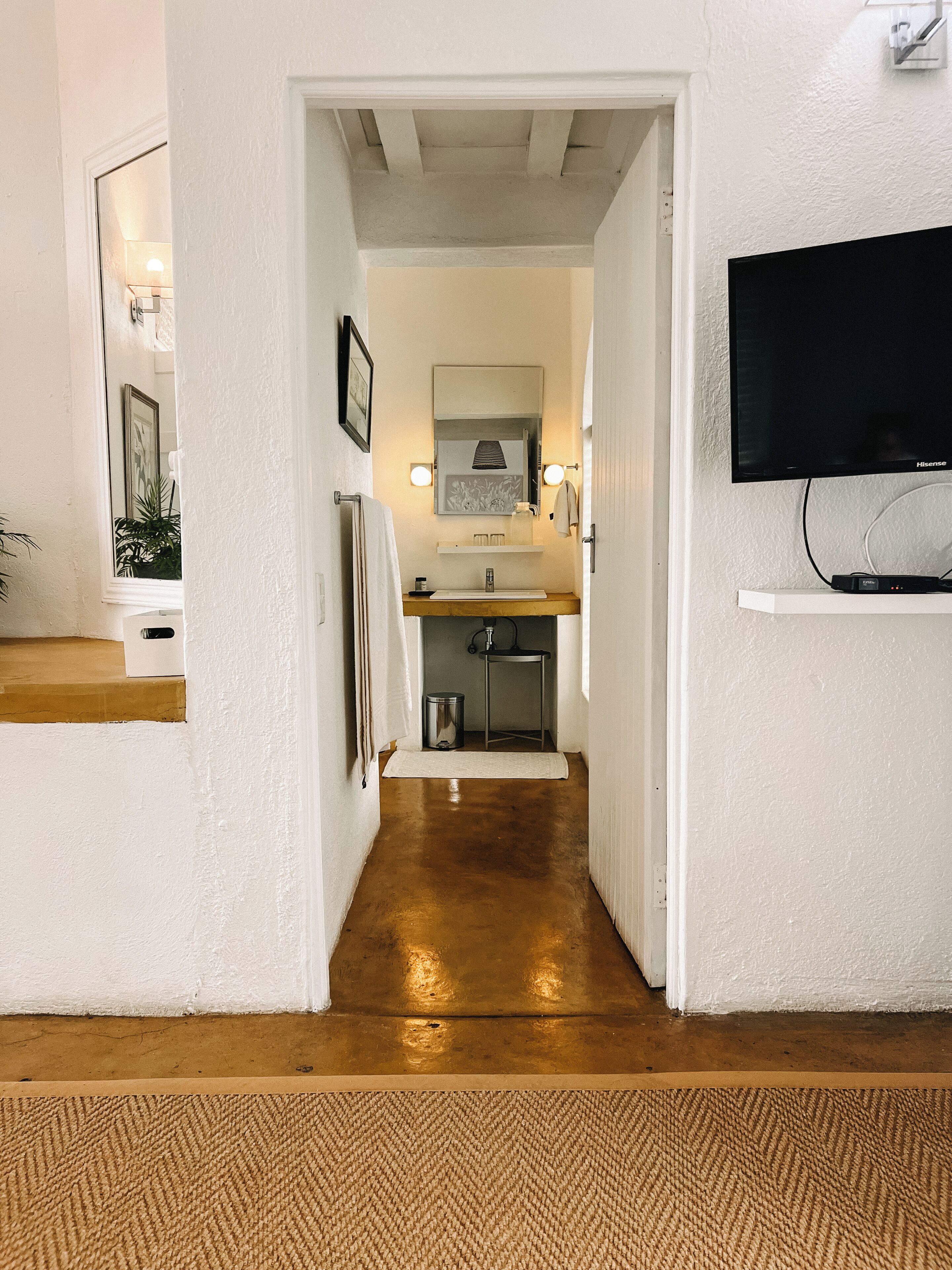 A hallway leading to a bathroom with a sink, mirror, and towel rack.