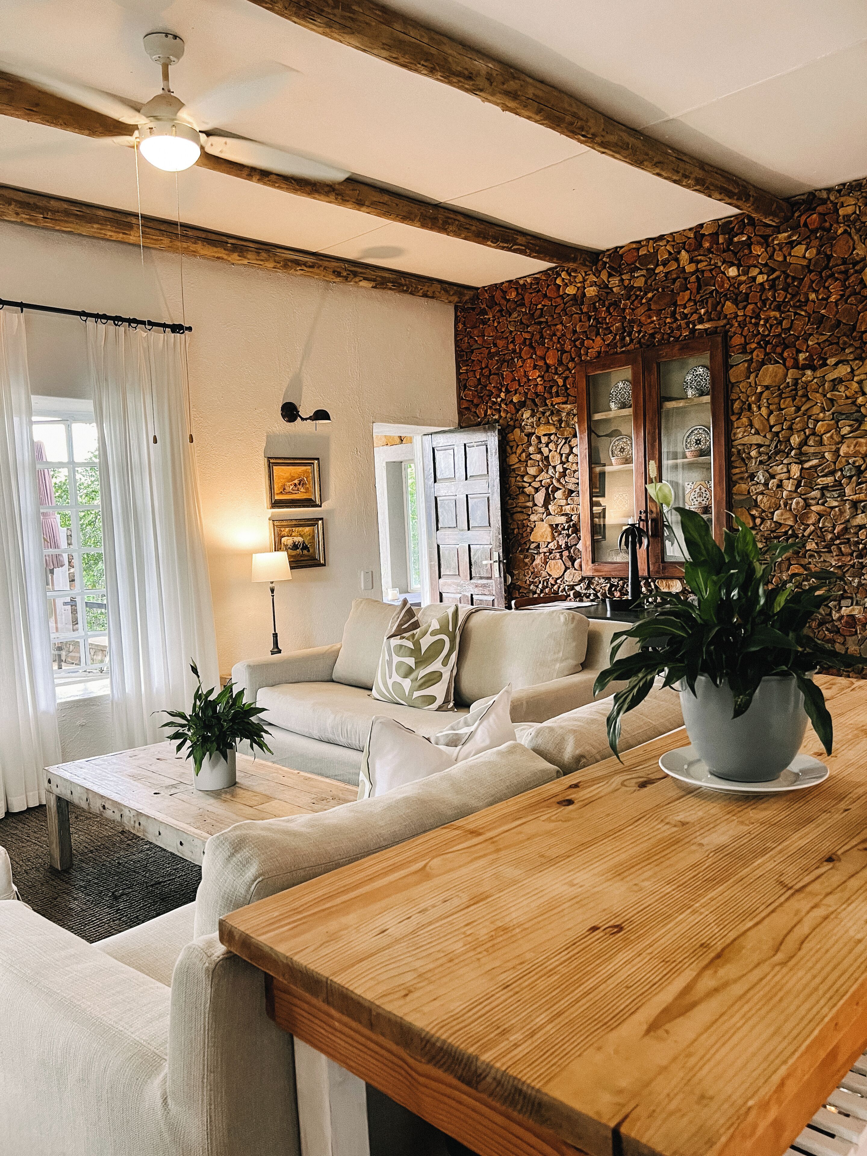 A living room with a wooden table, a sofa, a potted plant, and a stone wall.
