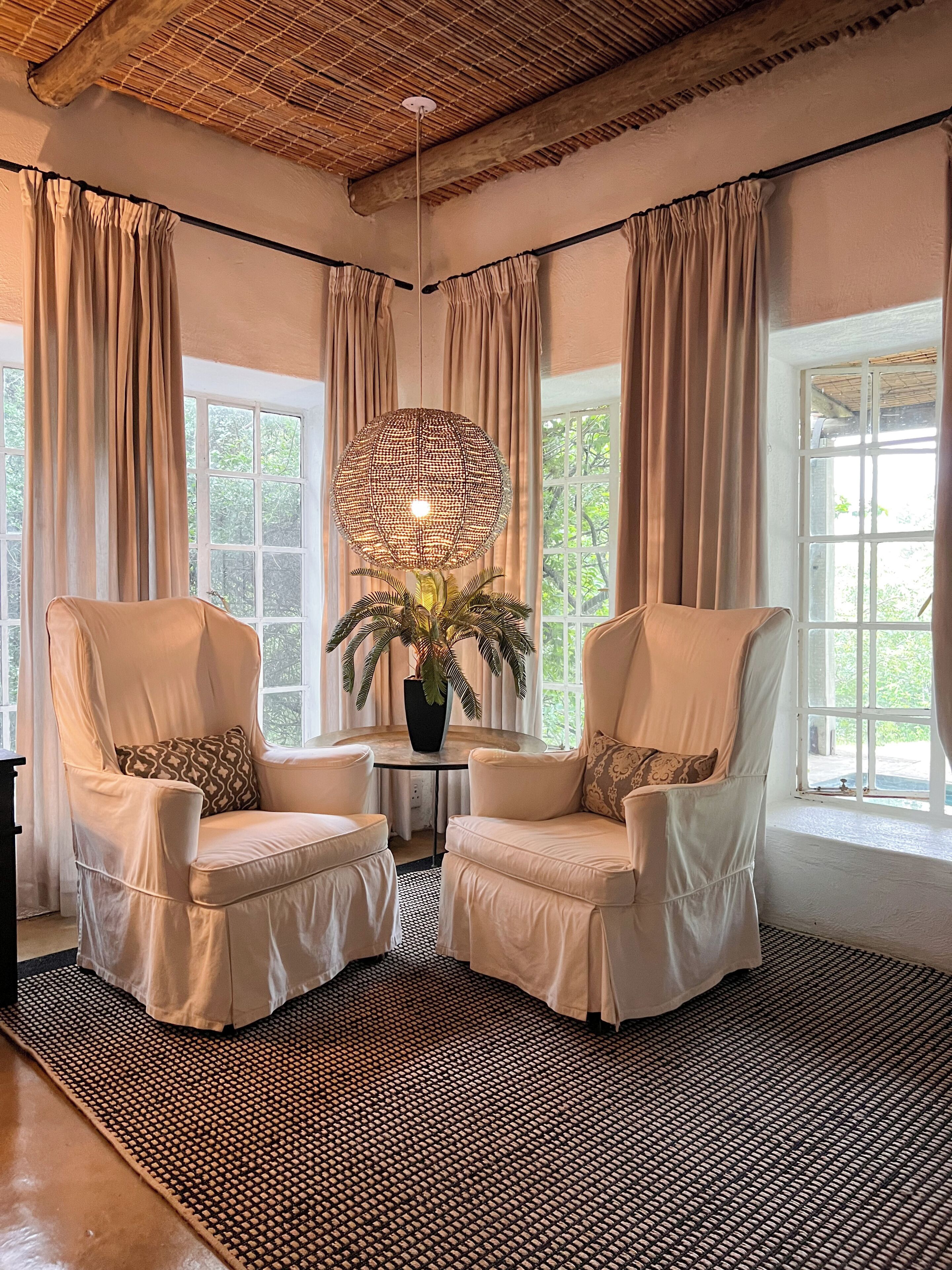 A room with two white armchairs, a round table with a potted plant, and a large woven lamp.