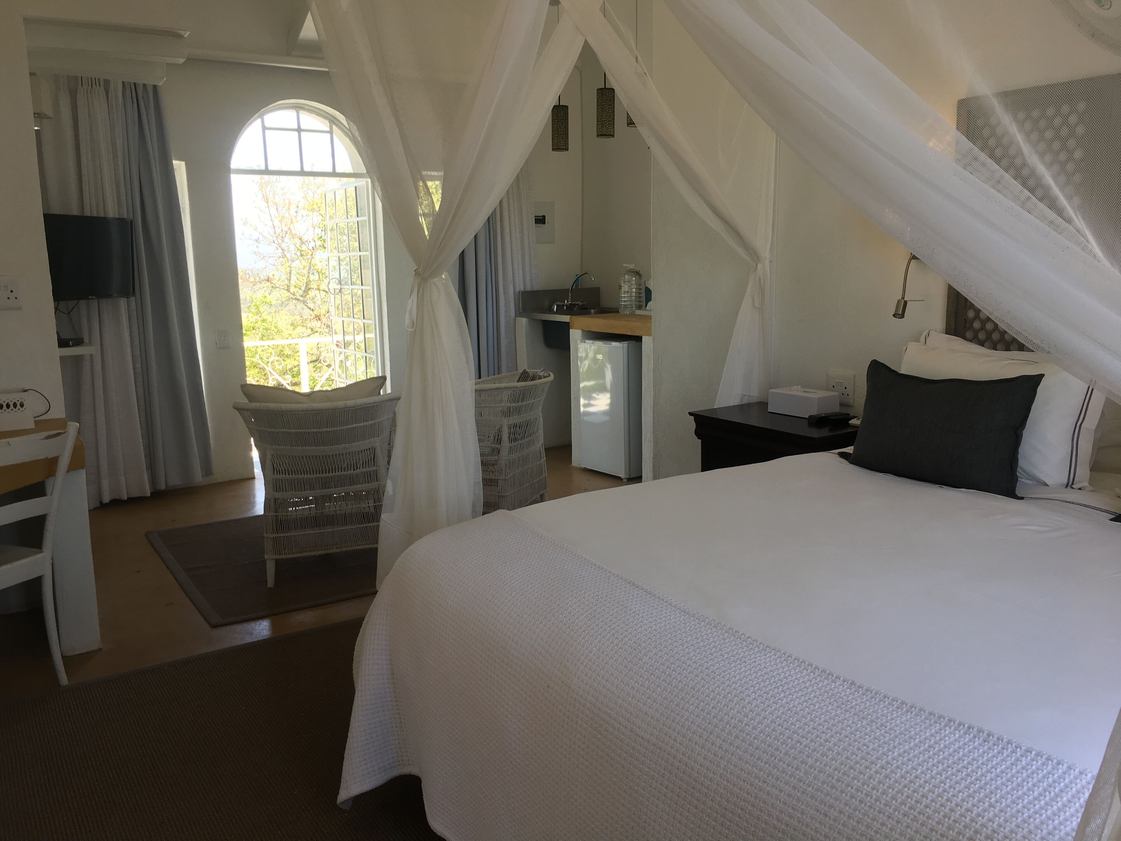 A bedroom with a large bed, a desk, a chair, and a small kitchenette.